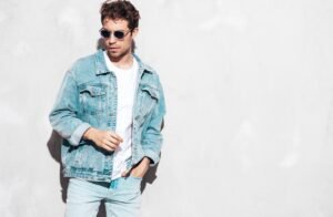 "Individual wearing a light denim jacket paired with summer attire, standing outdoors under the sun."