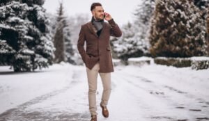 "Man wearing a denim jacket layered over fall attire, standing in a park with autumn foliage."
