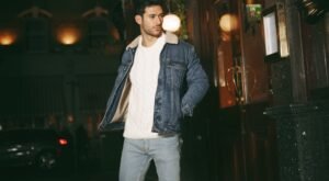 "Man wearing a casual outfit featuring a denim jacket and neutral-toned trousers, standing outdoors."